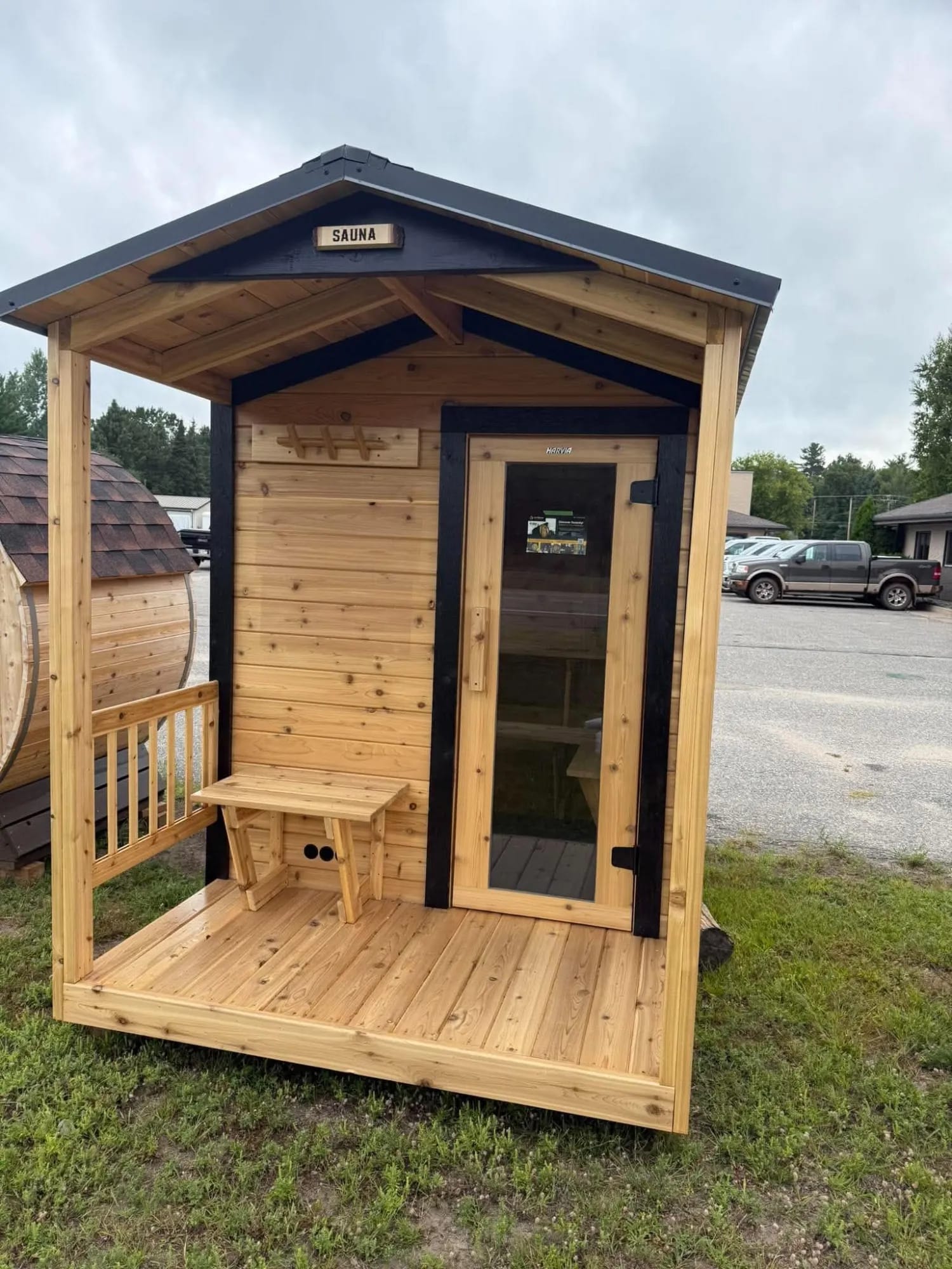 Cedar outdoor sauna with a covered porch, a bench and a glass door.